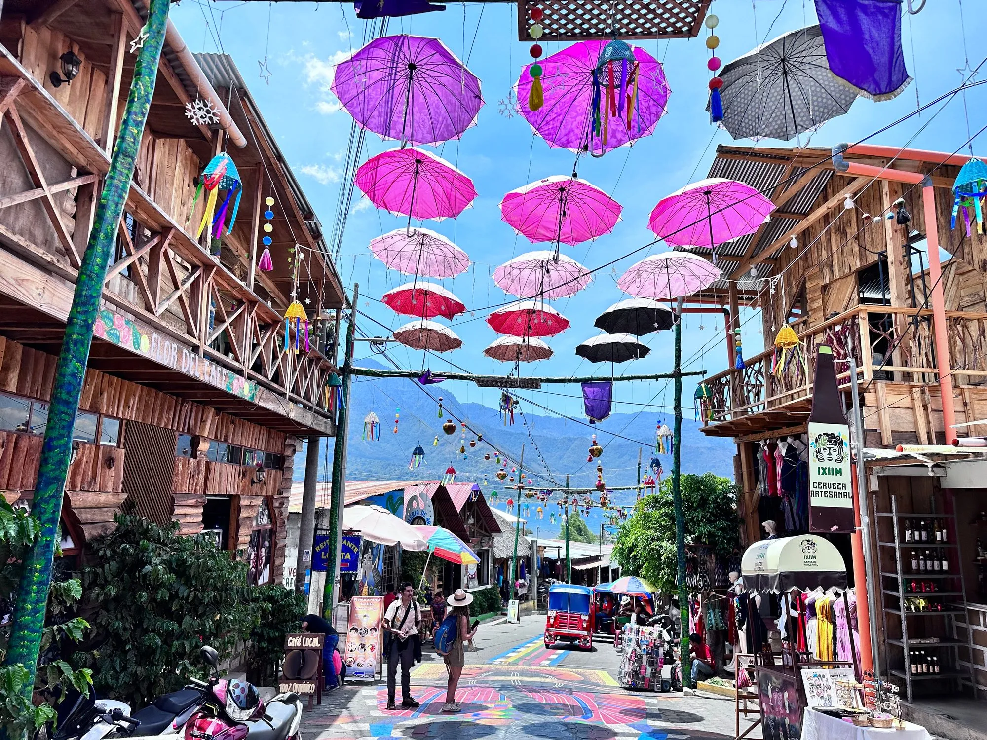 Rows of pink, purple and black umbrellas strung above a street decorated with colorful murals in San Juan La Laguna.