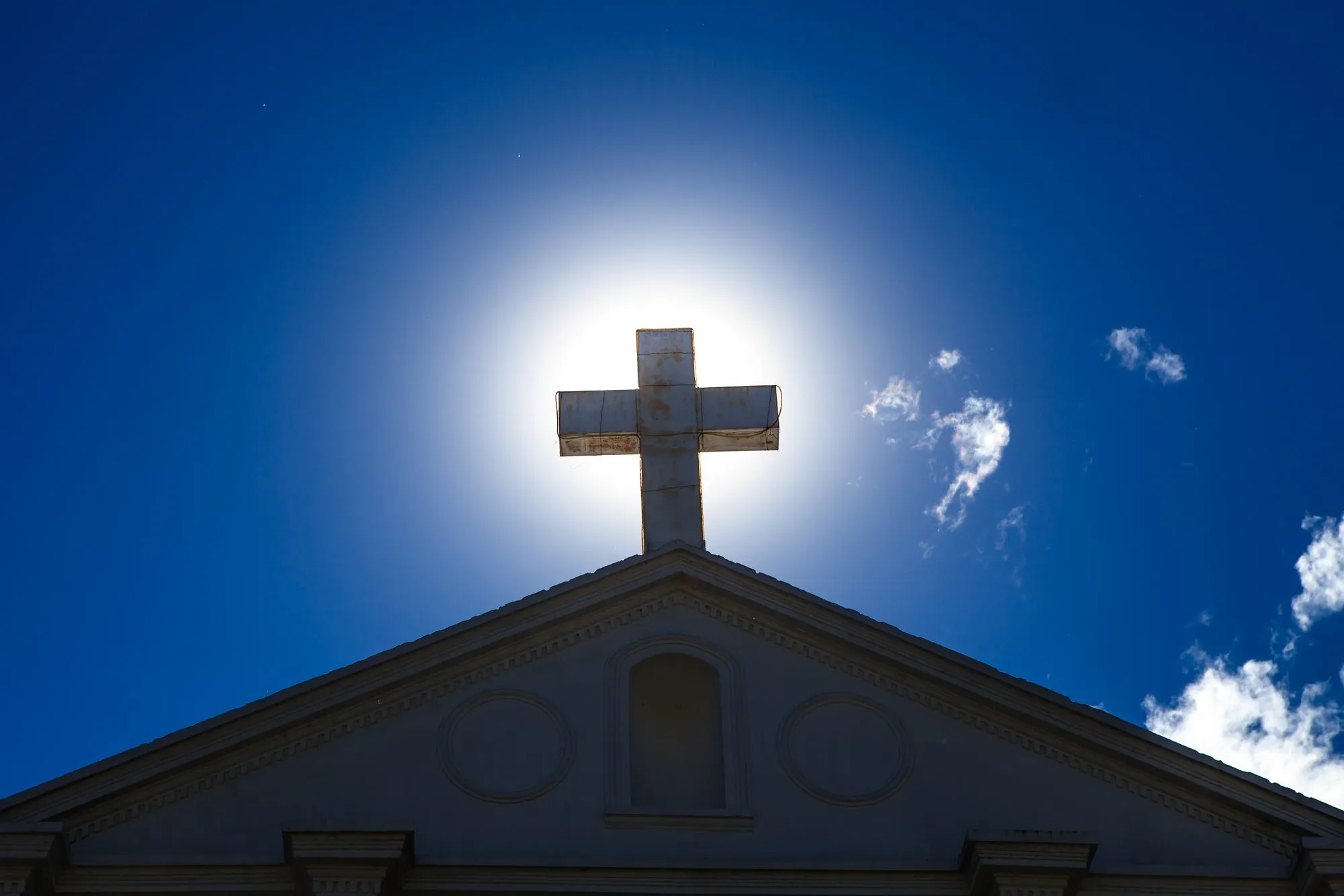 A white church cross silhouetted against the sky above a rooftop in San Pedro La Laguna.