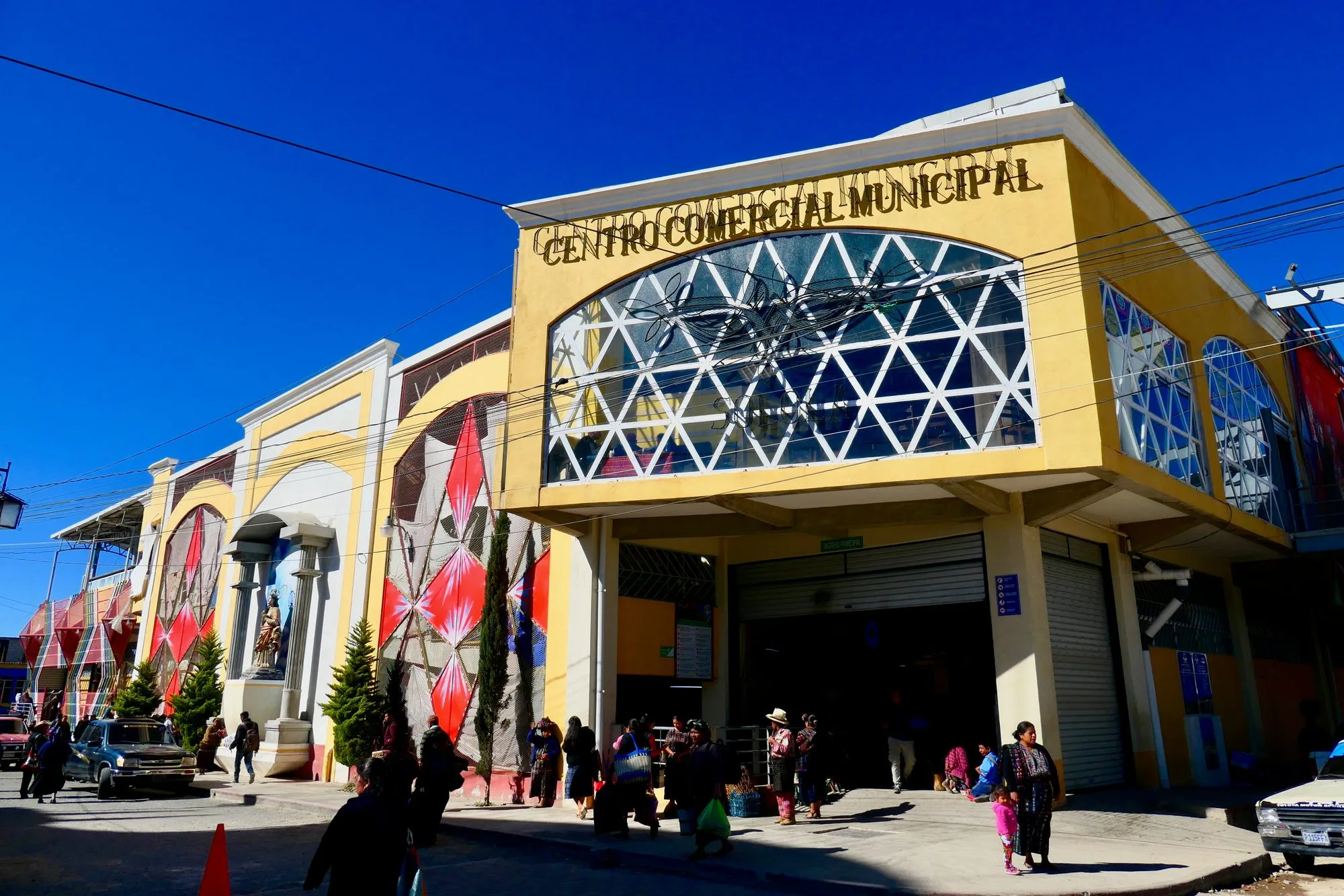 The yellow Centro Comercial Municipal market building in Solola, with shoppers in traditional dress outside its entrance.